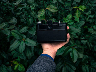Male hand holding a vintage film camera in the air. Green nature in the background.