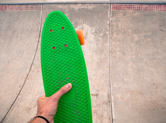 Male hand holding a green penny board in a skatepark.