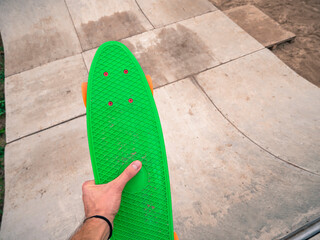 Male hand holding a green penny board in a skatepark.