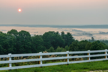 Fototapeta na wymiar Sunrise over fog and white fence