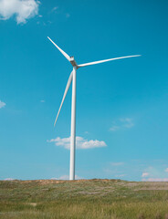 windmill on the background of the cloudy blue sky. Concept of alternative energy production from wind. Modern windmill with full-length blades. High quality photo