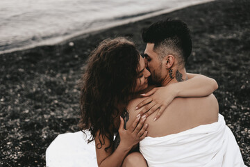 Fototapeta premium A couple in love are walking together hugging spend the night covered with a white blanket on the ocean beach on a romantic honeymoon in nature. Passionate man and woman of mixed diverse races