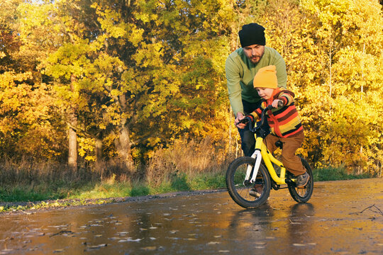 Cute toddler boy practicing cycling. Father teaches his little kid to ride bike in autumn park. Happy family moments. Time together dad and son. Candid lifestyle photo.