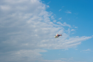 The helicopter is flying in the sky with clouds.