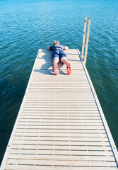 Boy lying on wooden pier over a lake watch fish in  blue water below