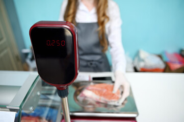 Soft focus on values on scales on the background of an out focus fishmonger weighing a salmon steak fillet on a scale.