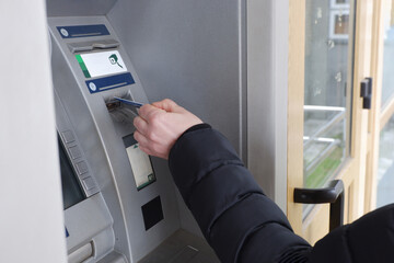 A man's hand inserts a credit card into an ATM machine.