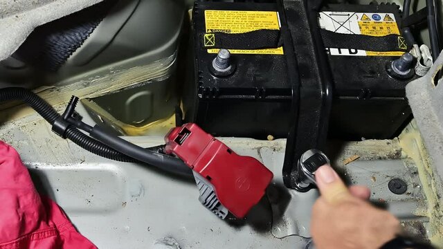 Car battery replacement with housing in the rear trunk. The electrician unscrews the fixing bolt of the battery housing bracket with a ratchet wrench.