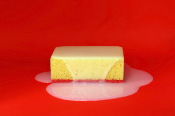Yellow sponge on a red background, liquid soap spreads on top of the sponge