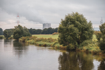 the nuclear power plant stands next to a wide river and white smoke rises from the cooling towers