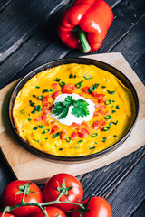 Homemade omelette with tomatoes and peppers, top view on a rustic wooden board 