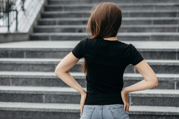 Stylish brunette girl wearing black t-shirt and glasses posing against street , urban clothing style. Street photography