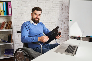 Handsome businessman sitting in a wheelchair and holding a clipboard