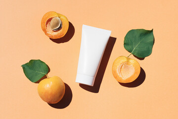 Blank white plastic skincare tube with fresh apricots fruit on pastel orange background. Natural cosmetic beauty product branding mock-up for brightening cream, body lotion, facial foam. Flat lay.