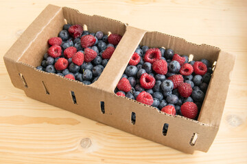 Fresh juicy ripe blueberries and raspberries are are in a cardboard box. Garden berries are mixed, closeup.