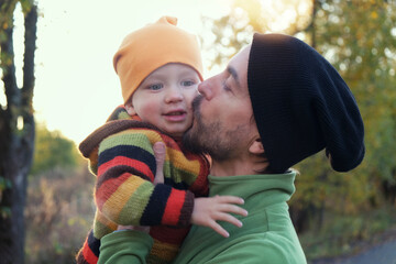 Father kissing his little child in autumn park at sunset. Happy family in fall season. Cute toddler boy and his dad together outdoor.