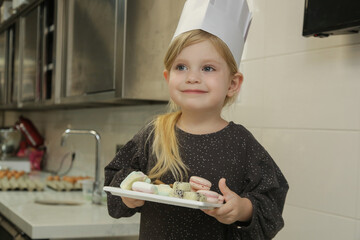 Happy little chef holding a plate full of sweets after successful cooking class.