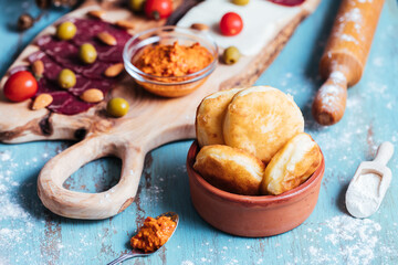Fried dough called Ustipci with olives, paprika cream and meat served on a wooden board