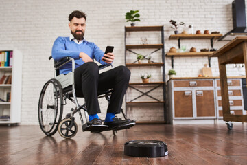 Man sitting in a wheelchair and using a robotic vacuum connected with a phone