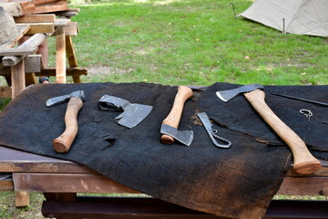 A close up on a set of equipment of medieval blacksmith or butcher including axes, machetes, pliers, and other weapons and tools arranged on a black cloth laying on a wooden table seen in Poland - obrazy, fototapety, plakaty