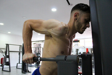 Fototapeta na wymiar young muscular caucasian guy training triceps exercise in gym