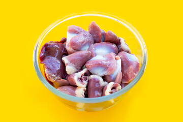 Mixed chicken entrails in glass bowl on yellow background.