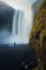 Moody view of female person standing in front of gigantic Skógafoss waterfall