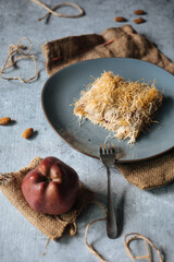 Turkish or Bosnian dessert called Kadaif or Kunefe served on a grey rustic background with apple