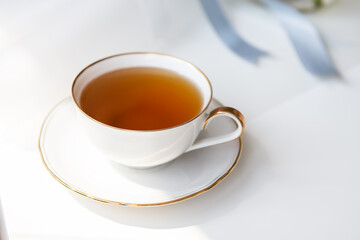 Black tea in a porcelain beautiful white cup with a gold cut. Beautiful sunshine. Tea ceremony.