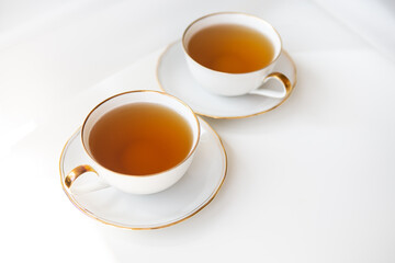 Two cups of tea. Black tea in a porcelain beautiful white cup with a gold cut. Beautiful sunshine. Tea ceremony concept.