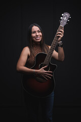 Fototapeta na wymiar Vertical of a beautiful young latina with a guitar in her hands and a black background.