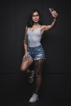 Beautiful woman with tattoos taking a picture of herself on a black wall