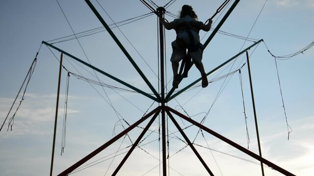 Back view of Teenage girl silhouette jumping on the trampoline against the blue sky