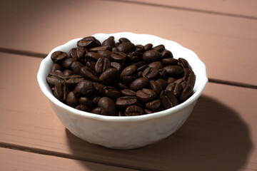 Coffee beans in a white plate on a wooden background. Coffee content, coffee shop.