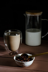 Coffee beans on the background of a cup of coffee and a carafe of milk.