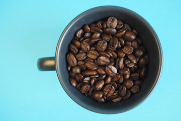 a dark mug filled with roasted whole coffee beans stands on a blue background. top view