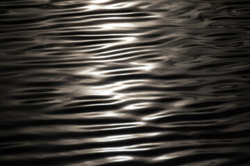 Metallic ripple water surface pattern. Shining in sun water with reflections. Wave texture close-up