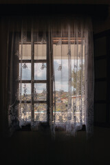 Fototapeta na wymiar View outside from Greek traditional house window with curtains on sunny summer Aegean sea coast village. Country house near Athens, Greece. Vertical