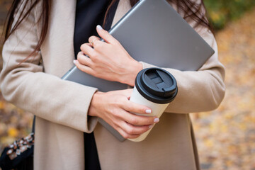 Brunette woman in autumn park with laptop and cup of coffee. Student. Teacher. Online education.