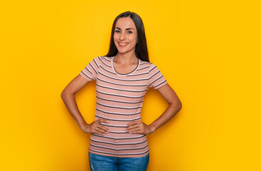 Happy confident beautiful young brunette woman in a t-shirt is posing and having fun isolated on the yellow background