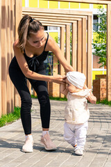 mom and toddler daughter walk in the city courtyard, child learns to walk