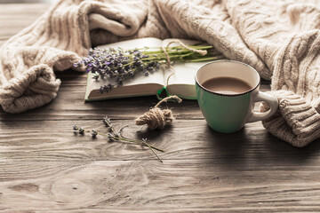 A cup of coffee on a wooden table, an open book and a warm sweater on the background of a bouquet of lavender flowers. Still life concept. Cozy morning.