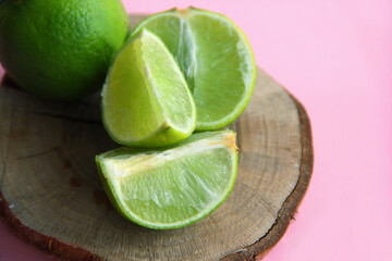 Lime and juicy lime slices on a wooden plate on a bright background