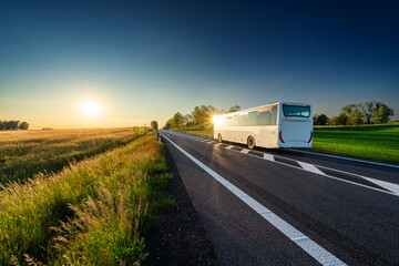 White bus reflective sun traveling on the asphalt road in rural landscape at sunset
