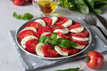 Italian caprese salad with sliced tomatoes, mozzarella cheese, basil and olive oil on light gray background.