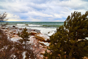 Nature landscape with dramatic sky and clouds, lake with ice, shore with snow and dark trees in...