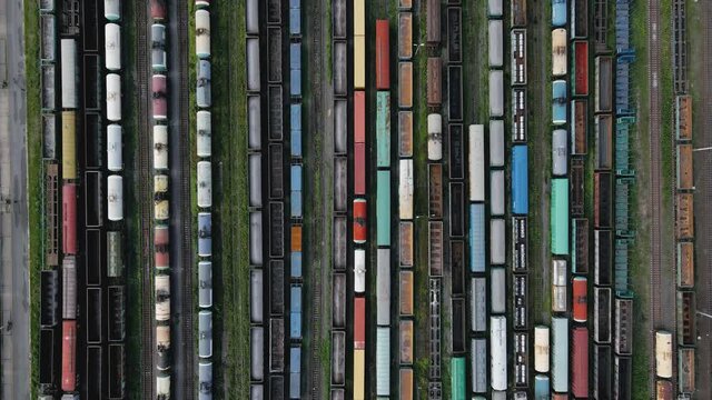 Aerial video from above of various colorful wagons on railroad. One train with freight wagons move forward. Cargo terminal. Import and export logistics. Delivery of goods by rail. View from the top.