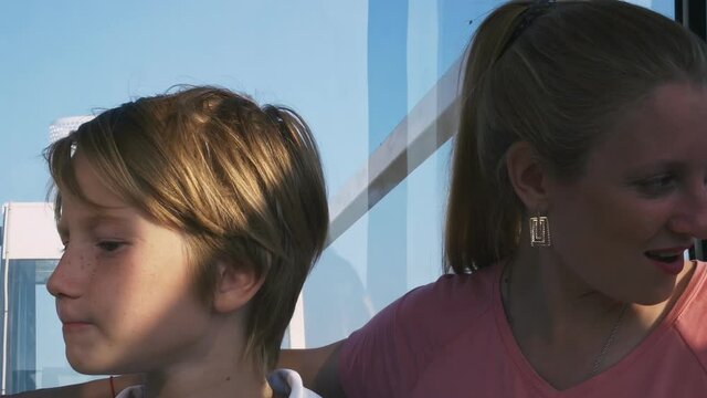 Fair-haired mom and son go up on the Ferris wheel discussing the view of the city, A beautiful woman with her son spend their free time at the attraction.