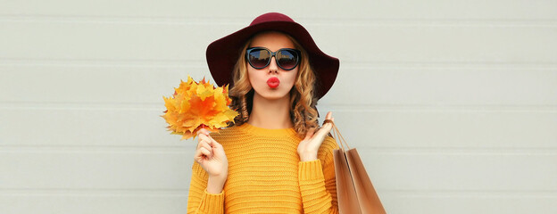 Autumn portrait of young woman with yellow maple leaves and shopping bags wearing a sweater and hat...