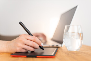 Graphic designer work with digital graphic tablet and laptop. Wooden workspace. Woman freelancer work from home office. Selective focus on pencil, blurred background. Close up photo.